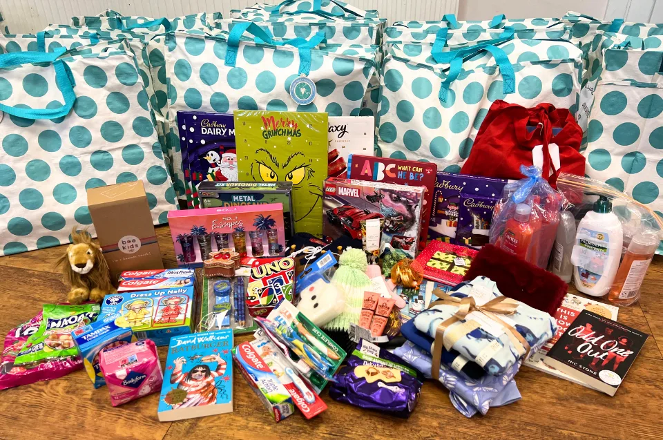 The contents of a Bromley Brighter Beginnings Christmas bag laid out on a floor: toys, books, games, pyjamas, toiletries, chocolate and an advent calendar, in front of a row of spotted bags