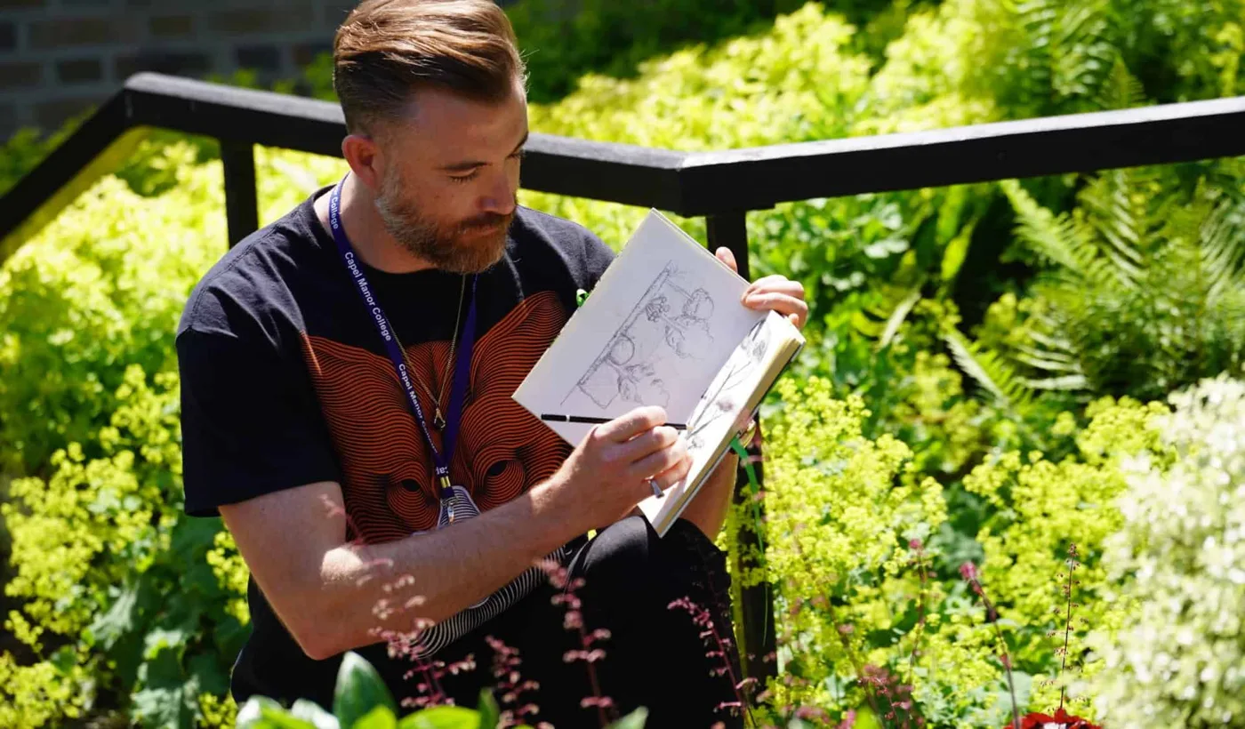 A Capel Manor College student sketching plants in a sketchbook among garden planting